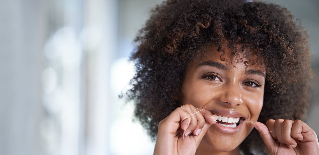 Getting those hard to reach places. Shot of a young woman flossing her teeth in the mirror.