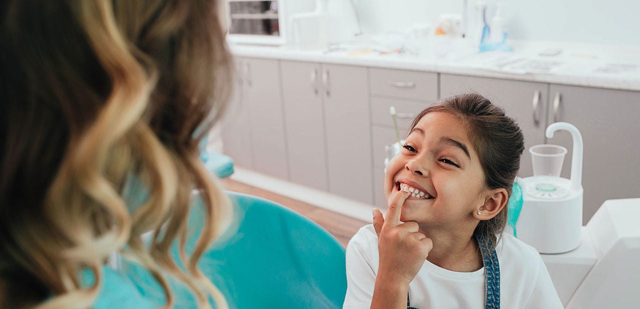 Mixed race little patient showing her perfect toothy smile while sitting dentists chair