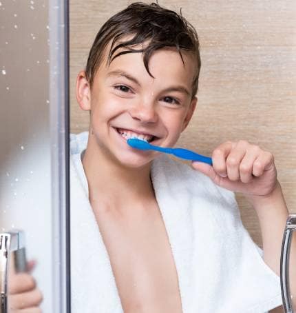 kid brushing teeth in front of mirror